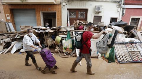 Dos personas cargan con sus pertenencias este lunes por una calle de Paiporta, en Valencia