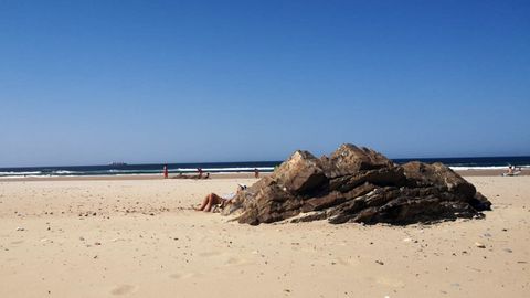 Una ba�ista se protege del vientro detr�s de una piedra en la playa de Xag� (Goz�n)