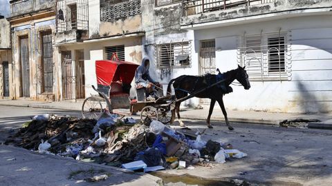 Un hombre en un carromato pasando ante la basura acumulada en una calle de Cuba