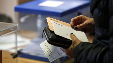 Una mujer con sus papeletas espera para votar en un colegio electoral de Oviedo