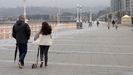 Una nia, junto a us patinete, pasea por el paseo de la playa, en Gijn