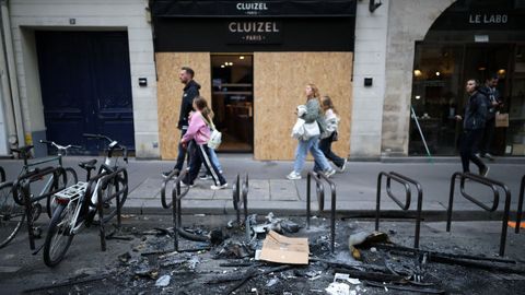 Gente pasando ante una tienda tapiada y una estaci�n de bicicletas quemadas en Par�s en las revueltas