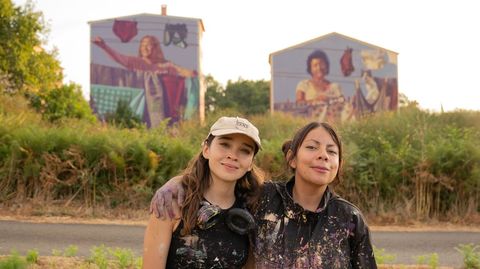 Las muralistas mexicanas Yuda (en la foto, con gorra) y Jan�n (con chaqueta) con las fachadas detr�s que pintaron cada una de ellas en el barrio de Conxo dentro de la �ltima edici�n del Delas Fest.
