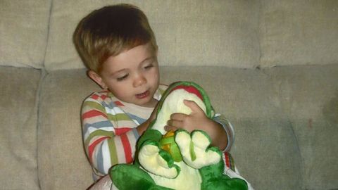 Foto de cuando era un nio pequeo con un peluche verde en las manos.