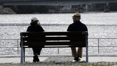 Una pareja de jubilados descansan en un banco en Viveiro
