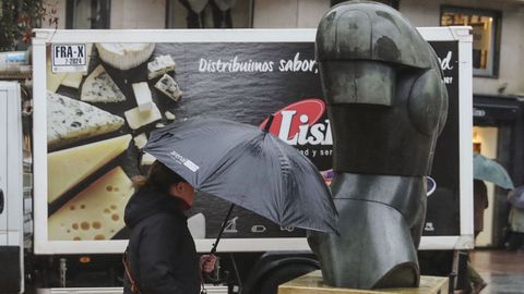 Una persona se protege de la lluvia en una calle del centro de Oviedo