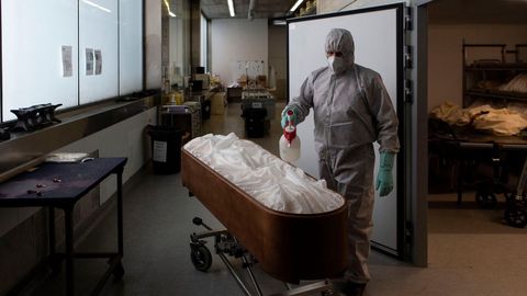 Un trabajador de una funeraria desinfecta el cuerpo de una persona fallecida con coronavirus
