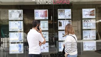 piso.Dos personas consultan los precios de los pisos delante de una inmobiliaria