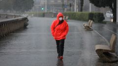 Una mujer pasea por el Paseo Martimo de A Corua entre la lluvia