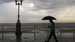 Un hombre se protege con el paraguas de la lluvia, en el paseo de muro de la playa de San Lorenzo de Gij�n, en una imagen de este verano
