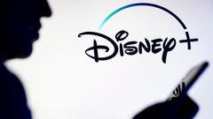 Un hombre consulta el m�vil ante un cartel con el logo de Disney+.