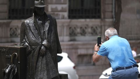 Un turista hace fotos a la escultura urbana conocida como El regreso de Williams B. Arrensberg con su espalda llena de sudor, este jueves en Oviedo