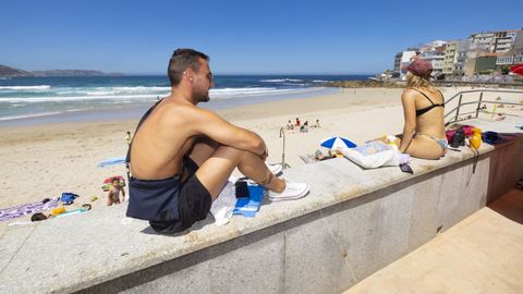 Dos jóvenes sentados sobre el muro de Area Maior, la playa urbana de Malpica