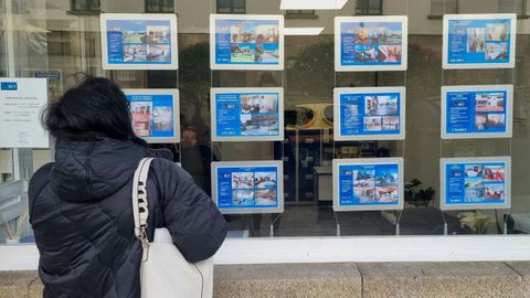 Una persona mira los anuncios de alquiler de viviendas en el escaparate de una inmobiliaria.