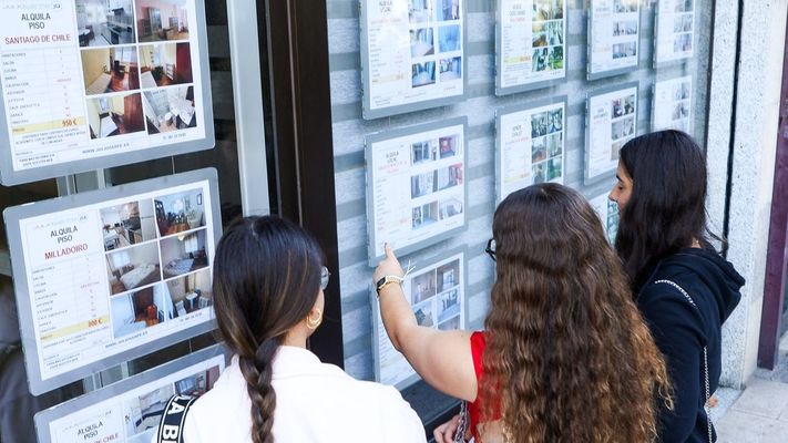 J�venes miran los anuncios de pisos en el escaparate de una inmobiliaria.