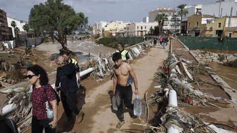 Varias personas transportan agua potable por uno de los puentes que cruza el barranco de Paiporta