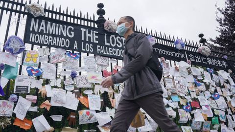 Un hombre camina con mascarilla por delante del homenaje a las v�ctimas del covid con la entrada de un cementerio en Nueva York