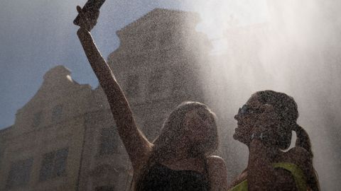 Dos turistas se refrescan bajo el agua que pulveriza un cami�n de nebulizaci�n durante un d�a caluroso y soleado en la Plaza de la Ciudad Vieja de Praga.