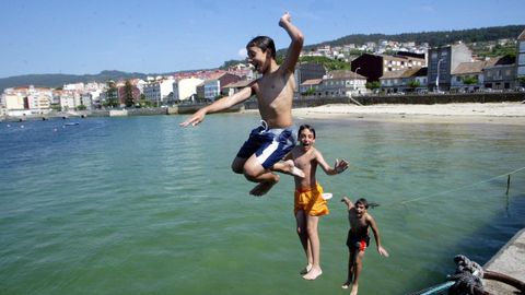 TRES JOVENES SE LANZAN DESDE EL MALECON AL AGUA EN LA PLAYA DE PESCADOIRA EN BUEU, PONTEVEDRA EN 2004.