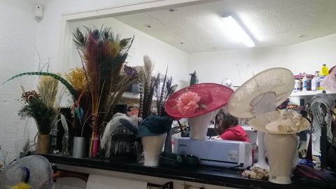 Plumas y pamelas elaboradas por Macarena, que al fondo trabaja en uno de sus diseños