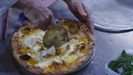 Un hombre corta una pizza con un cortador de acero inoxidable. 