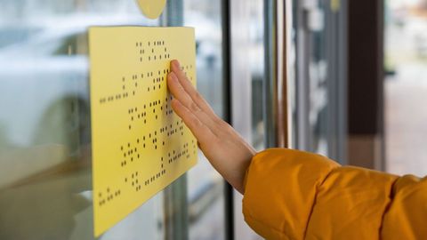 Una persona con dificultades de visi&oacute;n lee un cartel informativo en braille