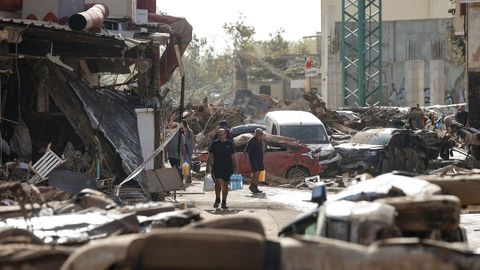 Varias personas caminan entre el lodo acumulado en las calles a causa de las intensas lluvias cadas por la fuerte dana