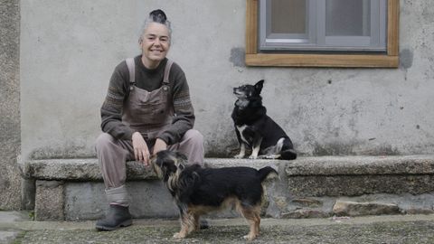 Cristina, junto a su perro Manu (abajo) y su perra Lupe, frente a la casa a la que se mud en el concello de Aranga.