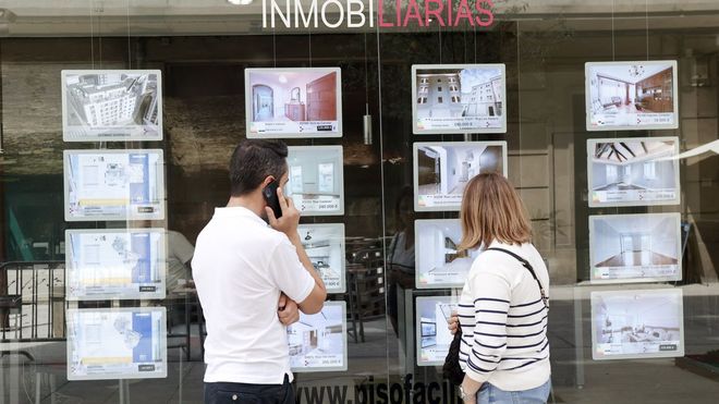 piso.Dos personas consultan los precios de los pisos delante de una inmobiliaria