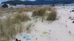 Decenas de bolsas y restos contaminantes enterrados afloran en la playa de Covas con el viento