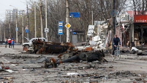 Un hombre, en bicicleta cerca de un tanque destruido 