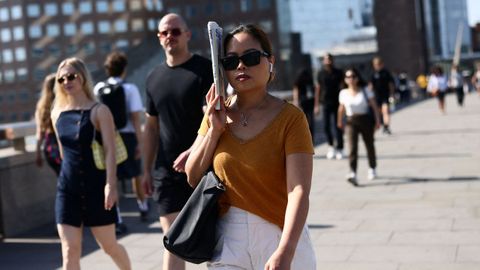 Una mujer se protege del sol con un peri�dico mientras cruza el puente de Londres (Reino Unido).