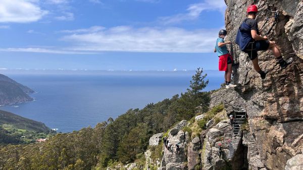 Dos escaladores con la aldea de Sa Andr&eacute;s de Teixido asom&aacute;ndose por la izquierda y el Atl&aacute;ntico de fondo
