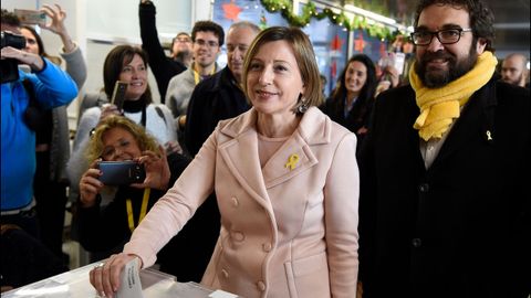 Carme Forcadell votando con un lacito amarillo en la solapa de su abrigo. 