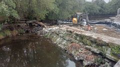 Una excavadora trabaja en las obras de derribo de la presa centenaria de Melide