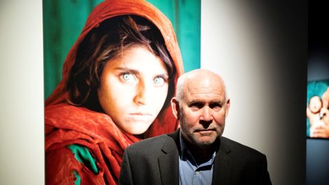 El fotógrafo estadounidense Steve McCurry posa junto a su legendario retrato de la niña afgana Sharbat Gula, que fue portada de «National Geographic».