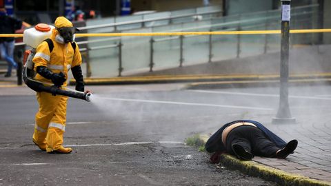 Un trabajador desinfecta a una persona que yace en el suelo, desplomada, en Quito