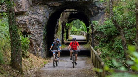 Dos personas en bicicleta pasan por uno de los t�neles sobre una antigua v�a de ferrocarril minero, situado en pleno trazado de la V�a Verde de la Senda del Oso. 