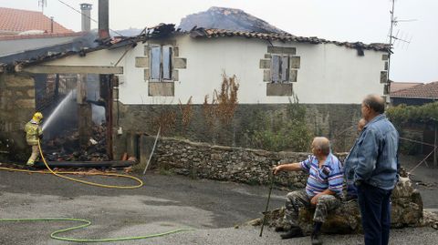 Unos vecinos de Budin observan este sbado los restos del incendio mientras los bomberos apagan los rescoldos de una de las casas que se quemaron