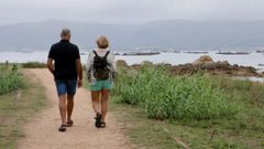 Unos paseantes por A Illa, con las bateas de fondo