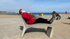 Una mujer descansa en un banco de la Barceloneta