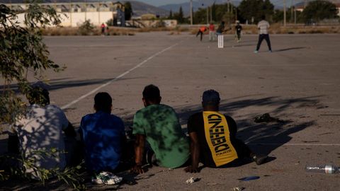 Un grupo de refugiados se entretiene jugando al criquet en una zona industrial de Atenas
