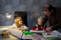 Un adulto ayuda a sus hijos a realizar los deberes en su domicilio.