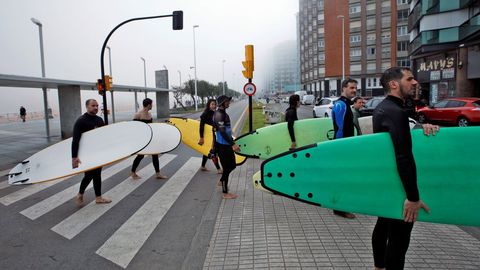 Un grupo de surfistas sale de la playa de San Lorenzo, en Gij�n, ante la espesa niebla