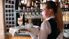 Una camarera con mascarilla sirviendo un caf� con leche