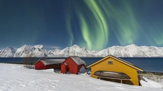 Aurora boreal sobre las casas de colores de Troms� en una noche nevada.
