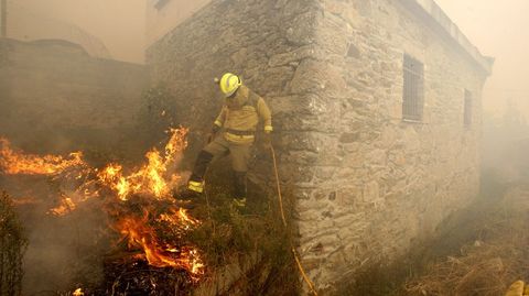 Un bombero forestal trata de apagar el fuego con sus botas junto a una casa de Frontn