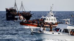 Un guardacostas llega al puerto de Lampedusa con migrantes rescatados, mientras son observados por turistas