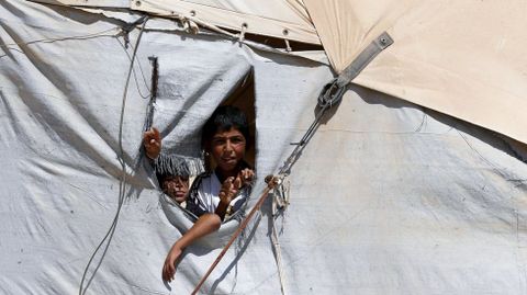 Niños sirios asoman sus cabezas por el hueco de una tienda en el campo de refugiados de Al Zaatari, que las Naciones Unidas establecieron en la ciudad jordana fronteriza de Mafraq