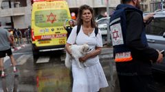 Una mujer israel huye con su perro entre los equipos de rescate, este lunes en Tel Aviv